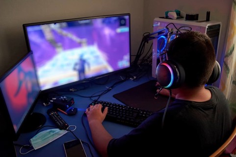 Back view of teenage gamer boy playing video games online on computer in dark room