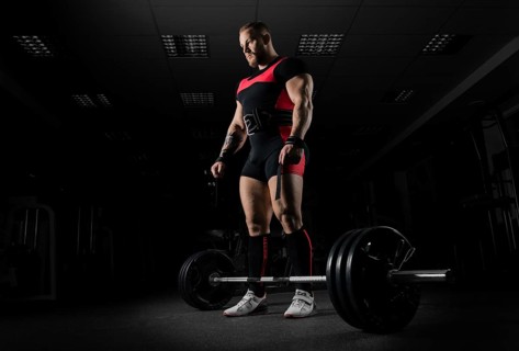 The weightlifter is preparing to perform an exercise called deadlift. He stands directly above the barbell and looks at it