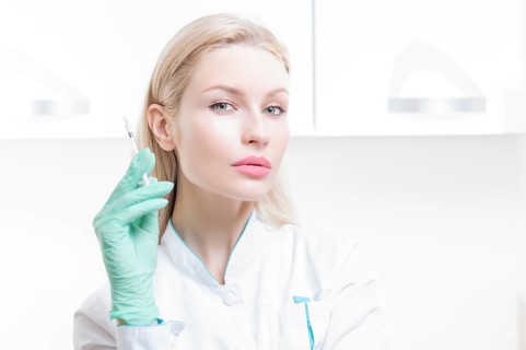 Portrait of a blonde girl in a medical gown with a syringe in her hands. Medical center advertisement.