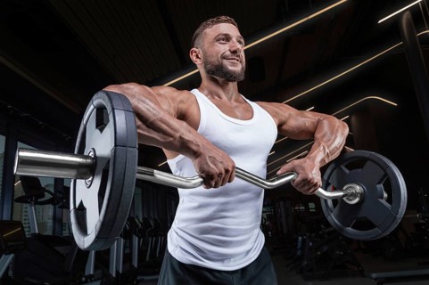 Handsome young man working out with a barbell in the gym. Shoulder pumping. Barbell pull to the chin. Fitness and bodybuilding concept