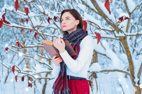 Portrait of a charming girl who reads a book in the winter forest. Concept of Christmas