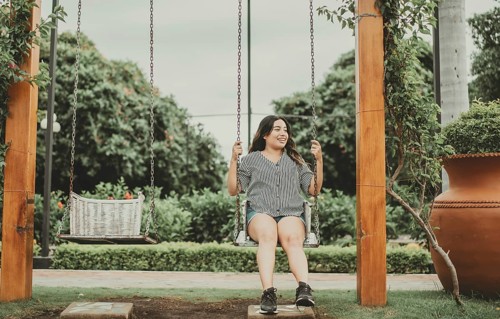 Happy young woman sitting on a swing in a beautiful garden. Portrait of smiling girl sitting on a swing in a garden