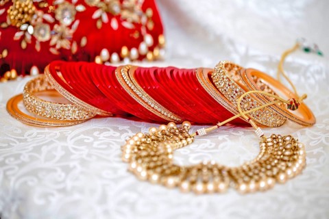 Elegant traditional Indian wedding jewelry with red bangles and gold accents on an embroidered fabric