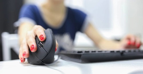 Girl's hand uses a vertical ergonomic joystick of a computer mouse. working at the computer