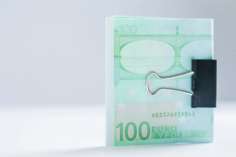Pack of euro notes lies on a white table fastened with a paperclip. The concept of savings during the crisis.