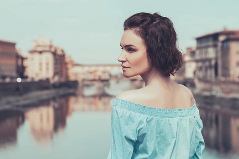 Portrait of a charming girl standing on a bridge in Florence. Arno River. View of the Ponte Vecchio. Tourism concept. Italy.
