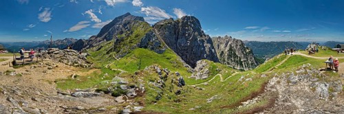 Panoramic view of a mountain landscape with hikers and green slopes under a blue sky