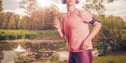 Portrait of a beautiful girl running in a sunny park in headphones with a smartphone. Music apps concept.