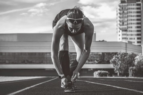 Image of a young female runner laces her shoes on a stadium track. Sports concept.