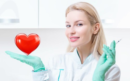 Portrait of a blonde girl in a medical gown. She holds a red heart in her palm. Concept of Cardiology and Transplantology.