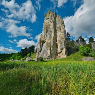 Striking limestone rock formation Burgstein with blue and white sky in the upper Altmuehltal surrounded by green vegetation
