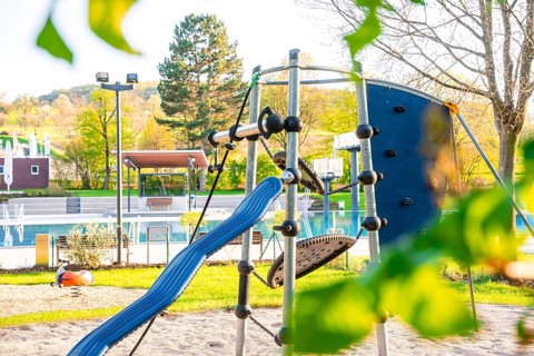 Children's playground with climbing frame and slide in the shade of trees