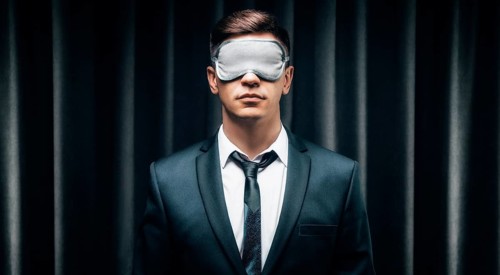 Portrait of a man in a mask for sleeping. He stands against the backdrop of a curtain. The concept of blind dates