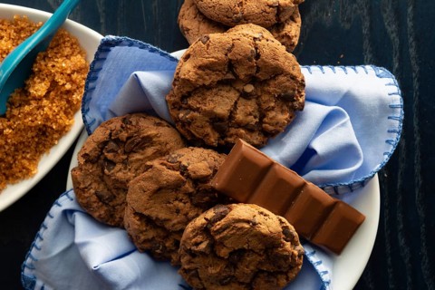 Chocolate chip cookies on a white plate beside brown sugar and a piece of milk chocolate