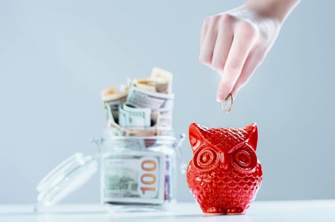 Female hand puts a coin in a piggy bank in the shape of an owl. Thrift concept.