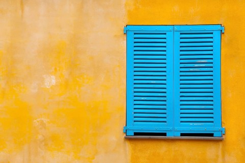 Blue shutter on yellow plaster wall
