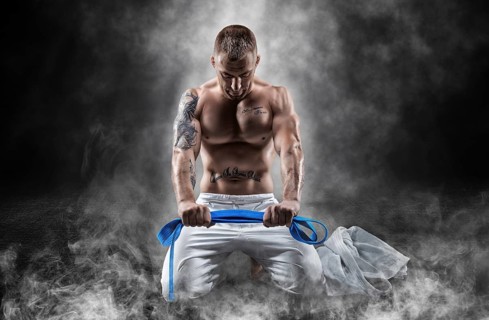 Professional wrestler sits in smoke with a blue belt in his hands and prays. The concept of mixed martial arts