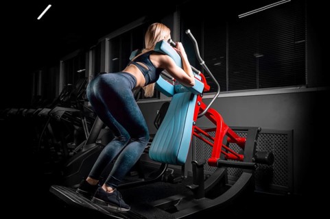 Charming blonde crouches in a hack machine. The concept of squat