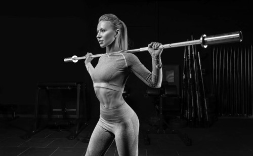 Beautiful tall blonde stands in the gym with a barbell on her shoulders. Squats. Fitness and bodybuilding concept.