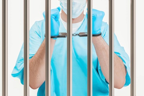 Doctor in handcuffs is standing behind a prison cell. The concept of corruption in medicine.
