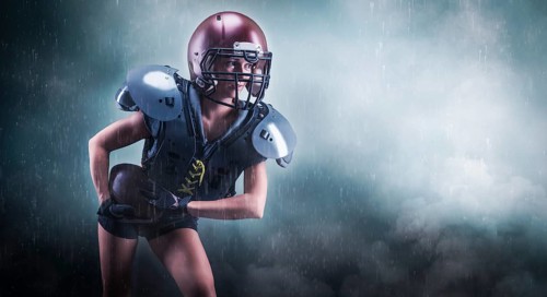 Image of a girl in the uniform of an American football team player. She runs with the ball against the background of light spots. Sports concept. Shoulders pads.