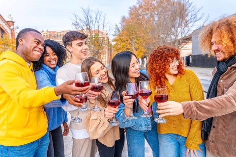 Multi-ethnic friends smiling and toasting with red wine in the street