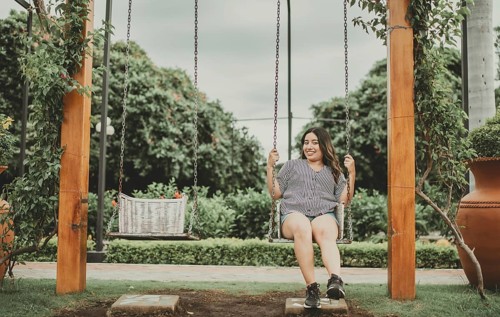 Portrait of smiling girl sitting on a swing in a garden. Happy young woman sitting on a swing in a beautiful garden