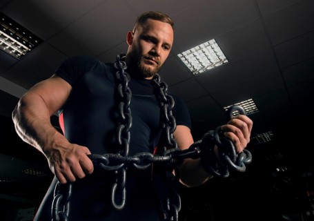 Professional powerlifter stands in the gym with iron chains wound around his arms