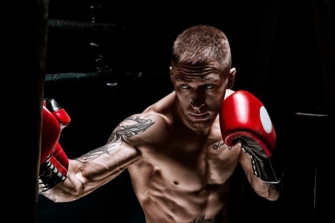 Professional boxer hits the bag against the background of the ring. Side view. The concept of sport and classic boxing.