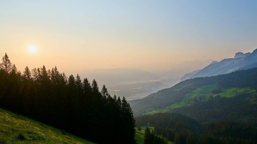 Sunrise over a misty mountain landscape with forest in the foreground