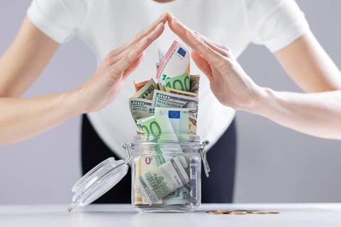Woman imitates a roof from her hands over a piggy bank full of cash notes. The concept of family thrift in a crisis.
