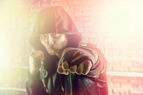 Boxer in a black sweatshirt and bandages wound on his hands beats his fist forward. The concept of sports