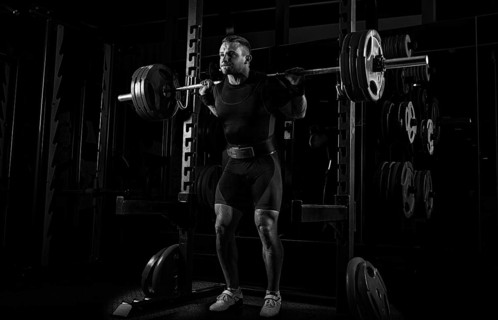 The weightlifter stands with a very heavy barbell on his shoulders. He is at the top and is preparing to sit down