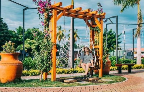 Beautiful girl in hat sitting on a white swing in a beautiful garden. Portrait of a smiling girl sitting on a swing in La Calzada