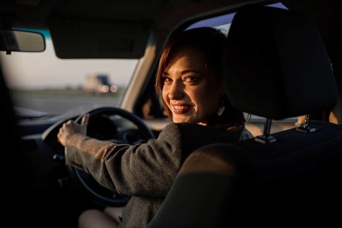Young beautiful smiling female taxi driver in a jacket greets passengers in a friendly manner