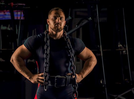 Handsome athlete with a chain around his neck stands in the gym and looks straight ahead