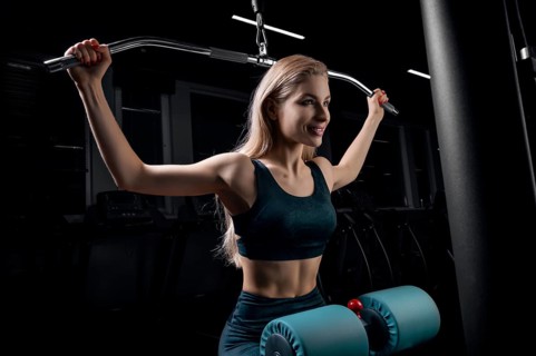 Charming blonde does exercises for the back in the gym. Neck pull for the head. The concept of sports