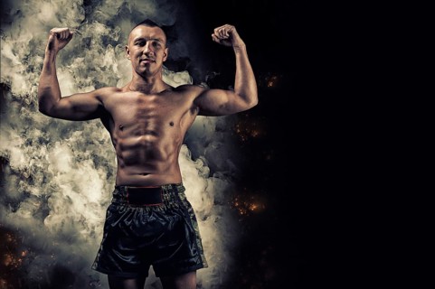 Portrait of a boxer of mixed martial arts standing against the backdrop of smoke and fire and celebrating a victory. The concept of sports