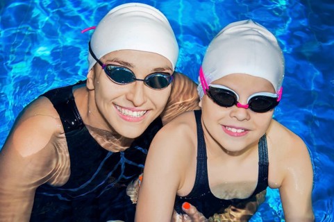Charming coach with his student swimming in the pool and smiling