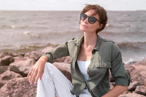 Portrait of a stylish woman sitting on stones in the bay. Windy weather. Happiness