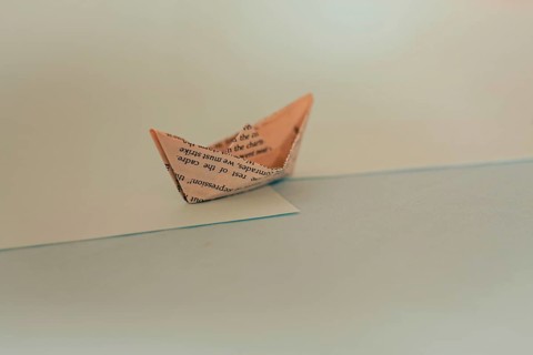 An origami paper boat with a minimalist design casting a shadow on a blue surface