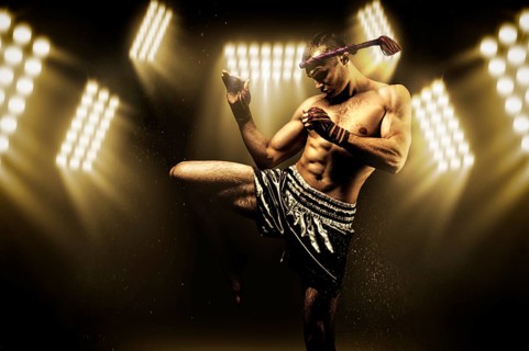 Kickboxer in the ring surrounded by searchlights stretches before the fight. Makes swing movements with his knee. Mongkhon.