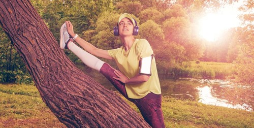Portrait of a beautiful girl running in a sunny park in headphones with a smartphone. Music apps concept.