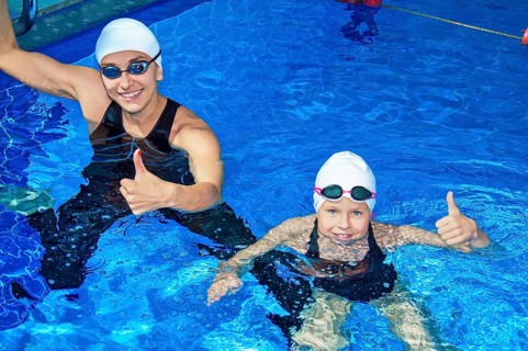 Charming coach with his student swimming in the pool and smiling