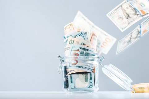 Glass piggy bank full of money. Banknotes are strewed from above. The concept of squandering.