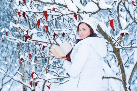Portrait of a charming girl who reads a book in the winter forest. Concept of Christmas