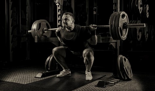 The weightlifter is getting ready to stand with a heavy barbell. Is at the bottom point