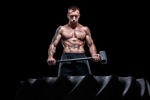 Professional sportsman stands with a sledgehammer in front of a rubber wheel. Functional training concept.