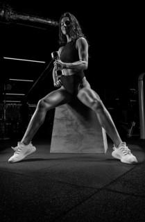 Tall athletic woman posing in the gym on a bench with dumbbells. Biceps pumping. Fitness and bodybuilding concept.
