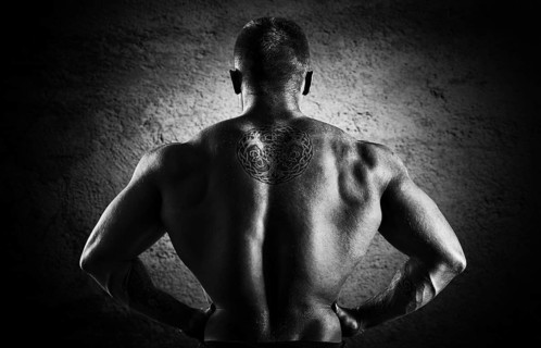 Huge weightlifter stands with his back to the camera and shows his huge back. Back view